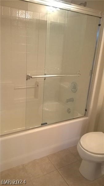 bathroom featuring enclosed tub / shower combo, toilet, and tile floors