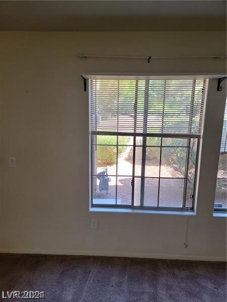 unfurnished room featuring a wealth of natural light and dark colored carpet