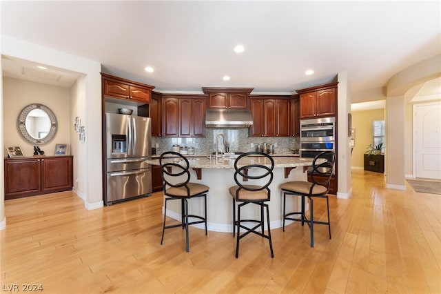 kitchen with light hardwood / wood-style floors, appliances with stainless steel finishes, tasteful backsplash, and a kitchen breakfast bar