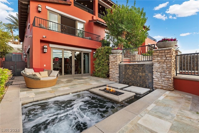 view of terrace with french doors, an outdoor fire pit, a balcony, and an outdoor hot tub