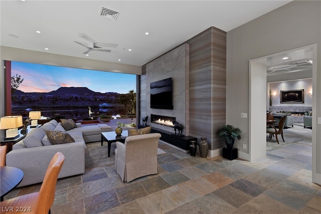 living room featuring ceiling fan, a large fireplace, and dark tile floors