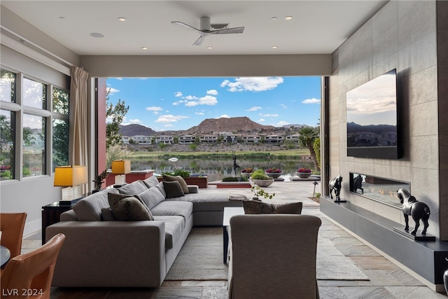 living room with tile walls, a tile fireplace, ceiling fan, and a water view