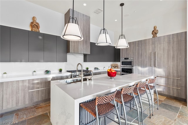 kitchen with pendant lighting, a large island with sink, light tile floors, sink, and double oven