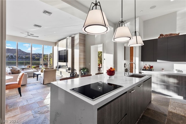 kitchen with tile flooring, black electric stovetop, an island with sink, decorative light fixtures, and sink