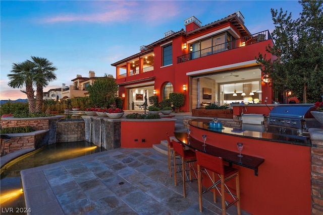 patio terrace at dusk featuring an outdoor bar, area for grilling, and a balcony