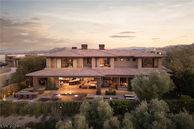 back house at dusk with a mountain view and a patio area