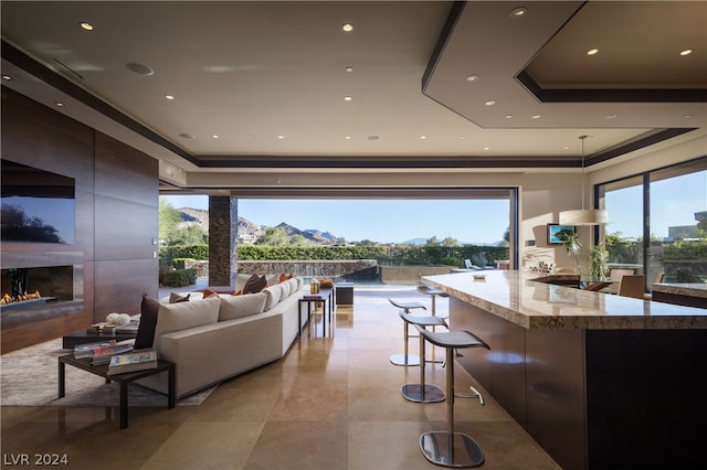 interior space with dark brown cabinets, hanging light fixtures, a tray ceiling, light stone counters, and light tile floors