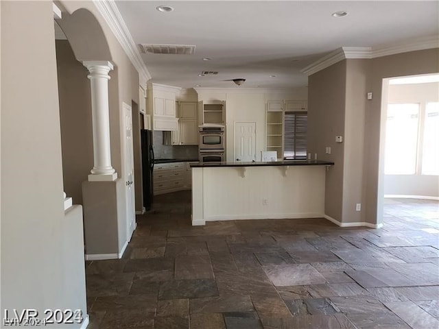 kitchen with black fridge, a breakfast bar, kitchen peninsula, and ornate columns