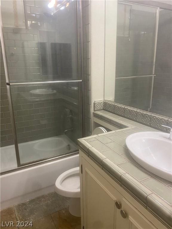 full bathroom with enclosed tub / shower combo, vanity, and toilet