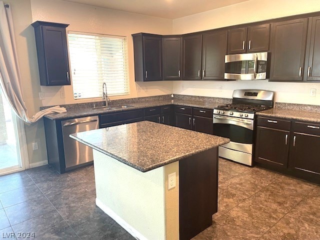 kitchen featuring appliances with stainless steel finishes, sink, a center island, and dark tile flooring