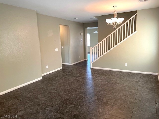 unfurnished room featuring dark tile flooring and a chandelier