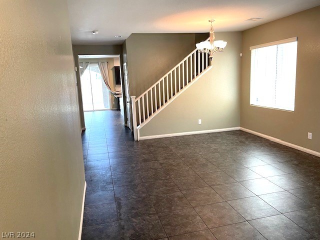 spare room with dark tile flooring and an inviting chandelier