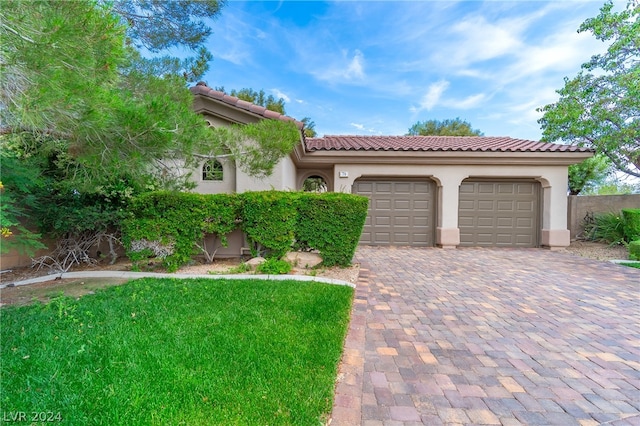 mediterranean / spanish house featuring stucco siding, a tiled roof, an attached garage, decorative driveway, and a front yard