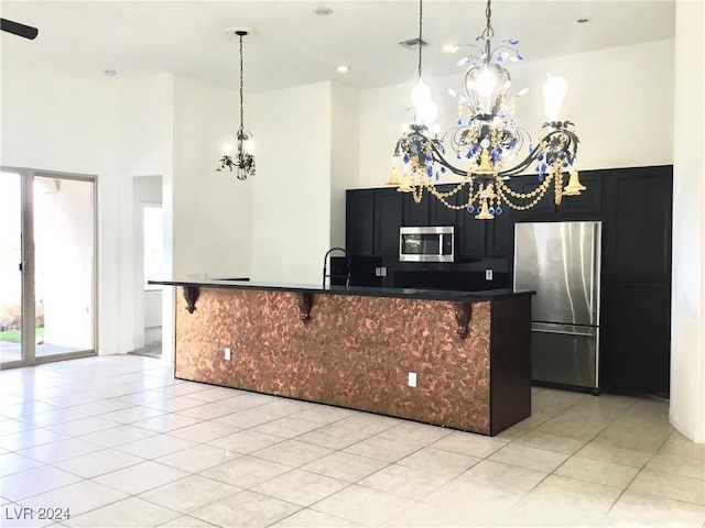 kitchen with a high ceiling, appliances with stainless steel finishes, dark cabinets, a chandelier, and a kitchen bar