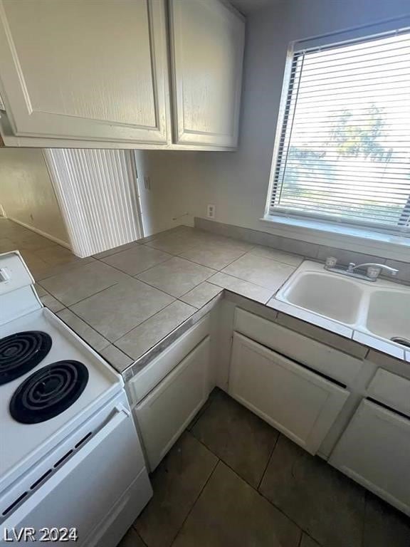 kitchen with dark tile flooring, tile counters, sink, and white electric range