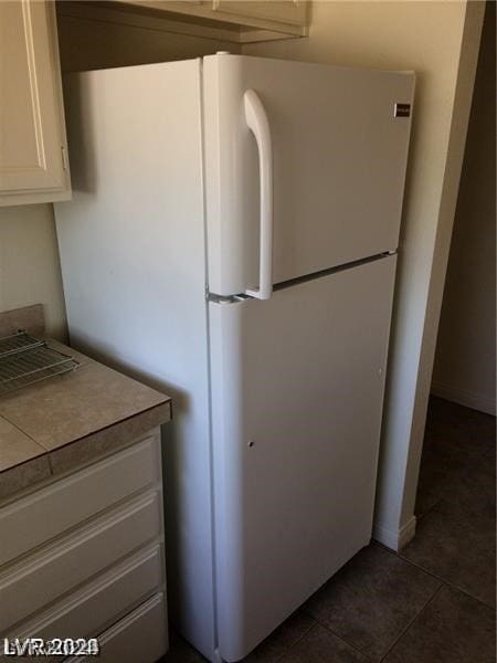 interior space with white refrigerator, dark tile floors, and white cabinetry