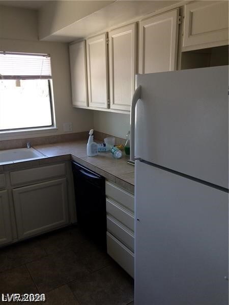 kitchen with dark tile floors, white cabinetry, white refrigerator, and black dishwasher