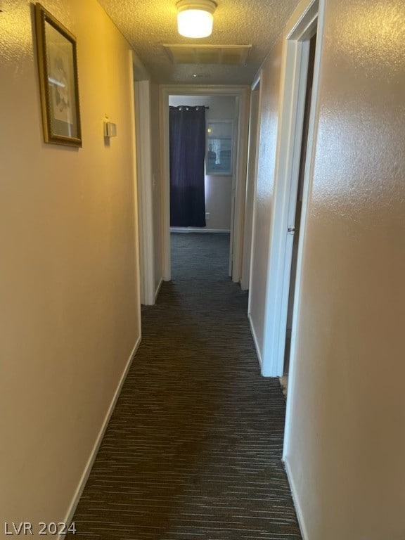 corridor with dark colored carpet and a textured ceiling