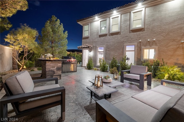 patio at night featuring area for grilling, outdoor lounge area, and exterior kitchen