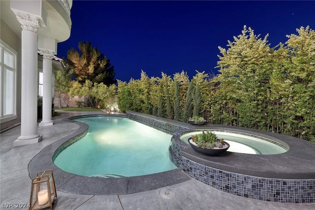 pool at twilight featuring an in ground hot tub