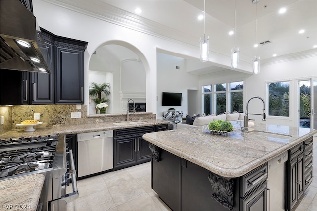 kitchen with appliances with stainless steel finishes, wall chimney exhaust hood, sink, and an island with sink