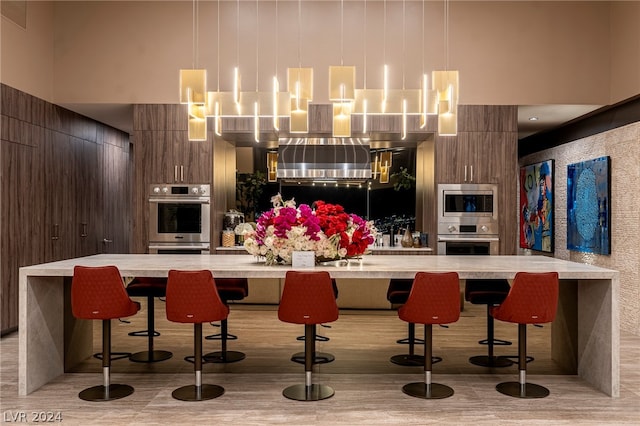 bar featuring appliances with stainless steel finishes, a high ceiling, light wood-type flooring, and hanging light fixtures