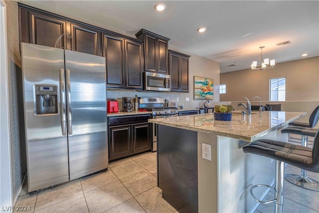 kitchen featuring a kitchen bar, decorative light fixtures, stainless steel appliances, a kitchen island with sink, and light tile floors