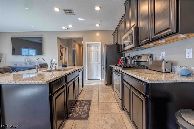 kitchen featuring dark brown cabinets, stainless steel appliances, a kitchen island with sink, sink, and light tile floors