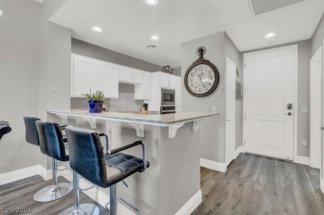 kitchen featuring appliances with stainless steel finishes, white cabinetry, hardwood / wood-style flooring, and light stone counters