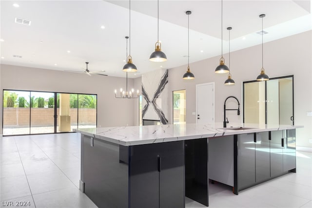 kitchen featuring sink, pendant lighting, ceiling fan, light stone counters, and a large island with sink