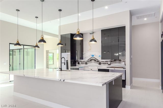 kitchen featuring light stone countertops, a large island with sink, decorative light fixtures, sink, and light tile patterned floors