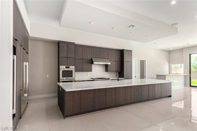 kitchen featuring a spacious island, light stone countertops, appliances with stainless steel finishes, sink, and light tile floors