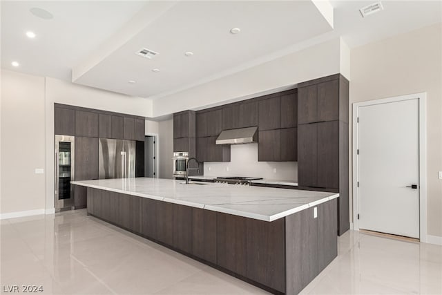 kitchen featuring wall chimney exhaust hood, a large island, and light tile floors