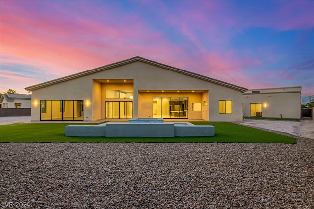 back house at dusk featuring a yard and a patio area