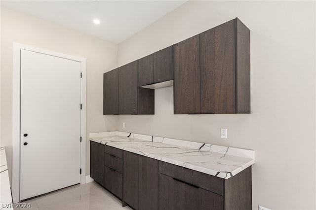 kitchen featuring light stone counters, dark brown cabinetry, and light tile floors