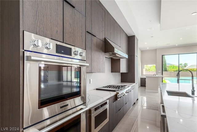 kitchen featuring light stone countertops, stainless steel appliances, wall chimney exhaust hood, sink, and light tile floors