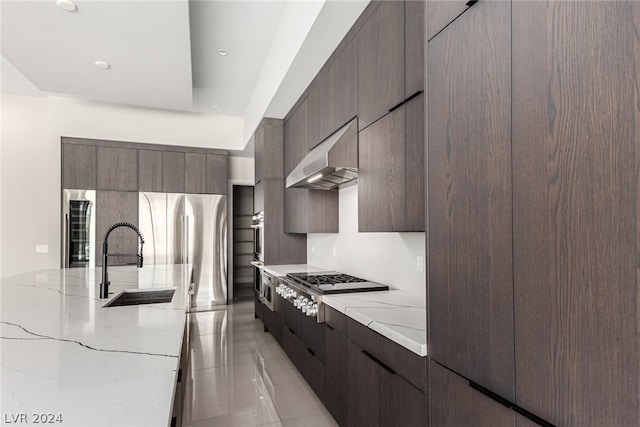 kitchen with light stone countertops, stainless steel appliances, wall chimney exhaust hood, backsplash, and sink