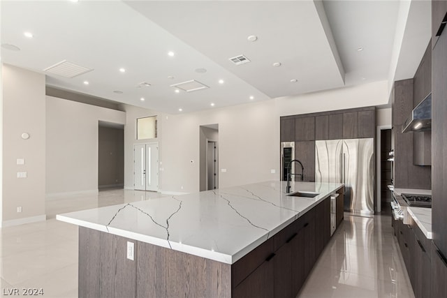 kitchen featuring light stone countertops, a large island, light tile floors, wall chimney exhaust hood, and sink