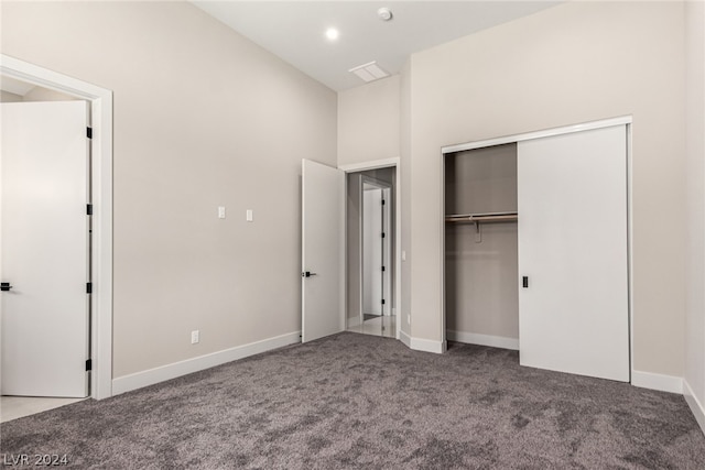 unfurnished bedroom with a towering ceiling, a closet, and carpet