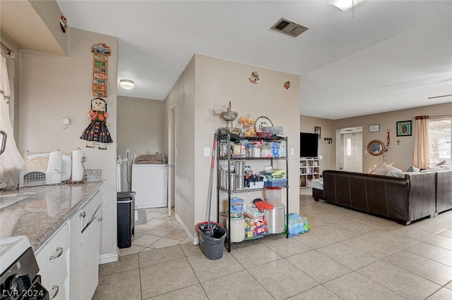 kitchen with light stone countertops, washer / clothes dryer, range, white cabinets, and light tile floors