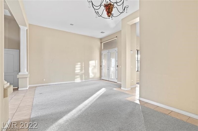 carpeted spare room with decorative columns and a notable chandelier