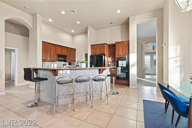 kitchen with a breakfast bar, black appliances, kitchen peninsula, a towering ceiling, and light tile floors