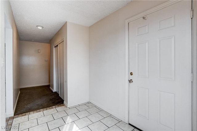 interior space with light tile patterned floors, baseboards, a textured ceiling, and light carpet