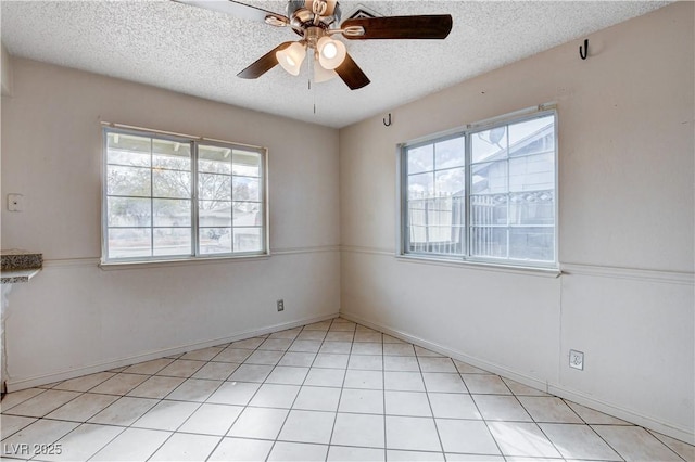 empty room featuring a ceiling fan, baseboards, a wealth of natural light, and a textured ceiling