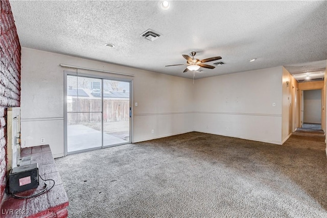 carpeted empty room featuring visible vents, a textured ceiling, a wood stove, and a ceiling fan