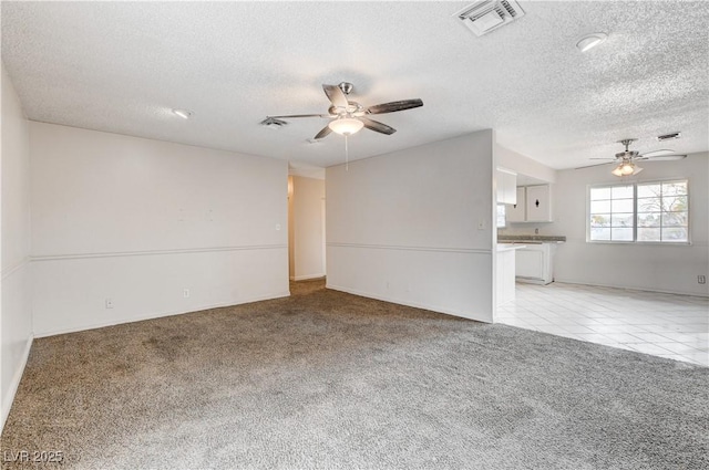 spare room with visible vents, light carpet, light tile patterned floors, a textured ceiling, and a ceiling fan