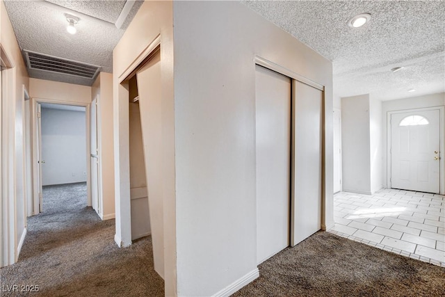 hallway featuring visible vents, a textured ceiling, and carpet floors