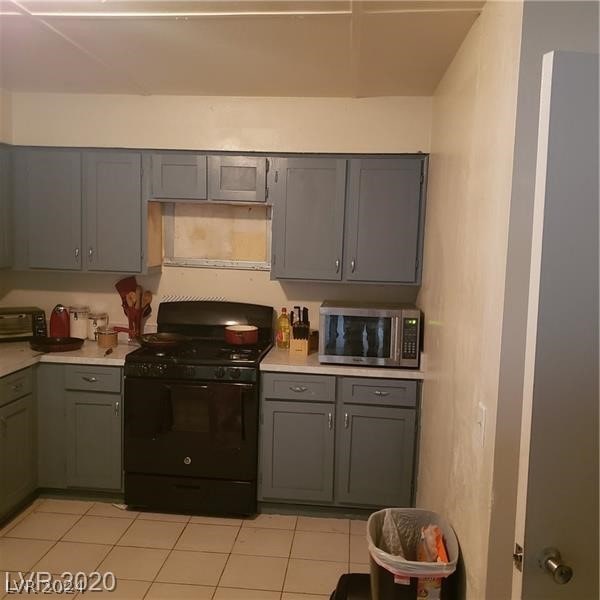 kitchen with wall chimney range hood, light tile floors, and black gas stove