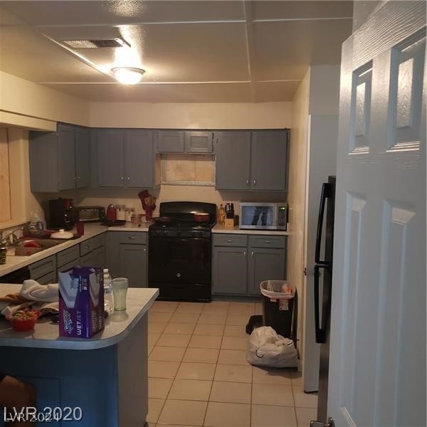 kitchen with stainless steel microwave, sink, gray cabinetry, and black range oven