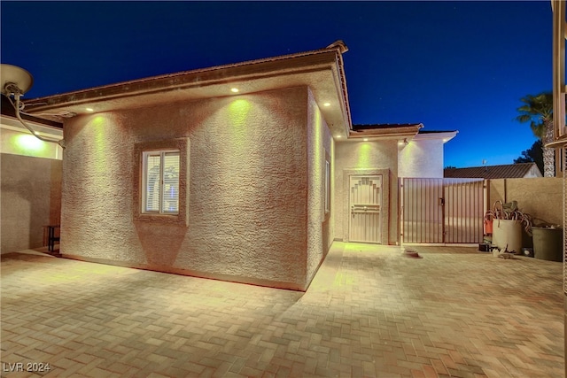 property exterior at twilight with fence, a gate, and stucco siding